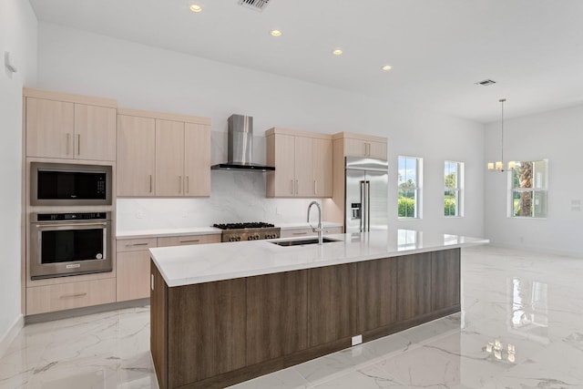 kitchen with light tile patterned floors, wall chimney range hood, an island with sink, built in appliances, and sink