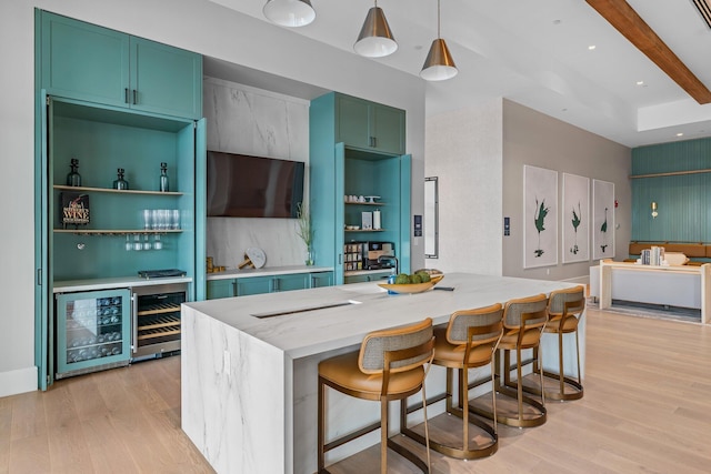 kitchen with decorative light fixtures, light stone countertops, light wood-type flooring, and beverage cooler