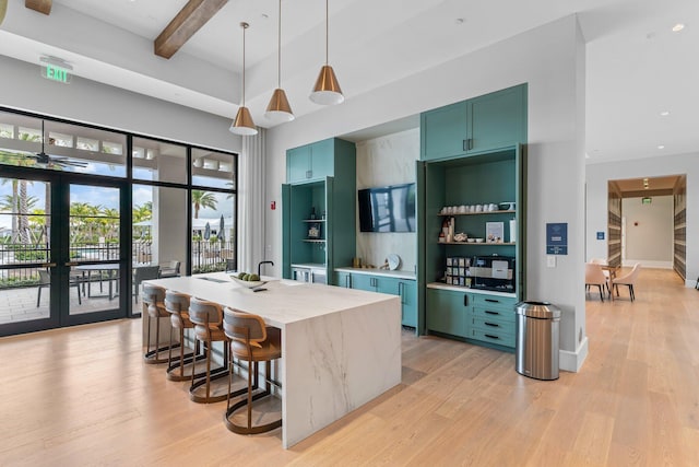 kitchen featuring light stone counters, decorative light fixtures, a kitchen island with sink, light wood-type flooring, and beam ceiling