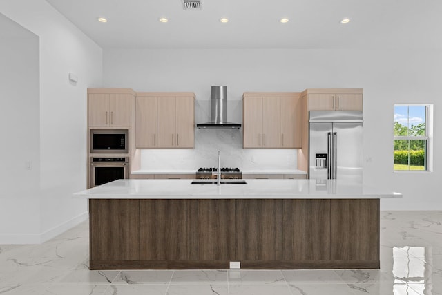 kitchen with wall chimney range hood, built in appliances, a kitchen island with sink, and light tile patterned floors