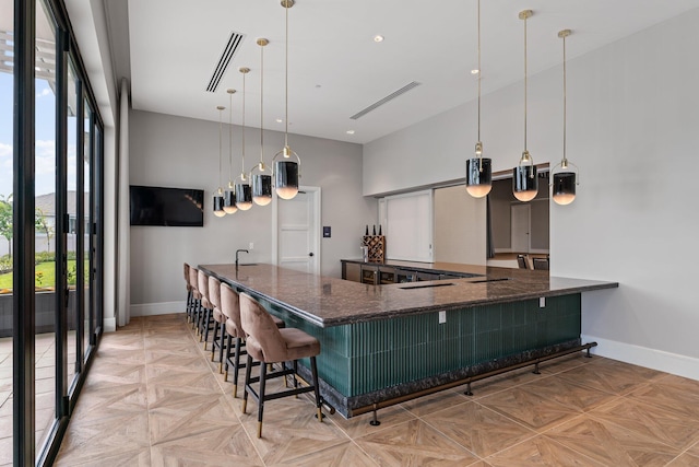 kitchen with a kitchen bar, dark stone counters, kitchen peninsula, decorative light fixtures, and light parquet floors