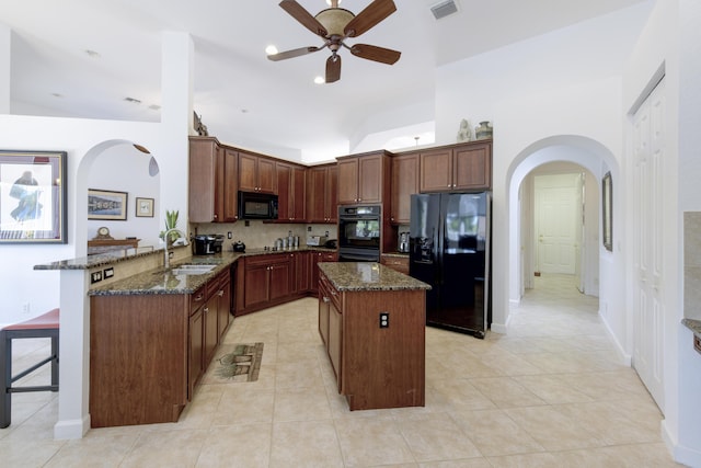 kitchen with dark stone countertops, black appliances, a center island, kitchen peninsula, and a kitchen bar