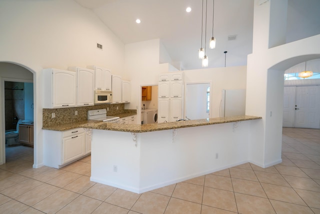 kitchen with dark stone countertops, white appliances, decorative light fixtures, high vaulted ceiling, and tasteful backsplash