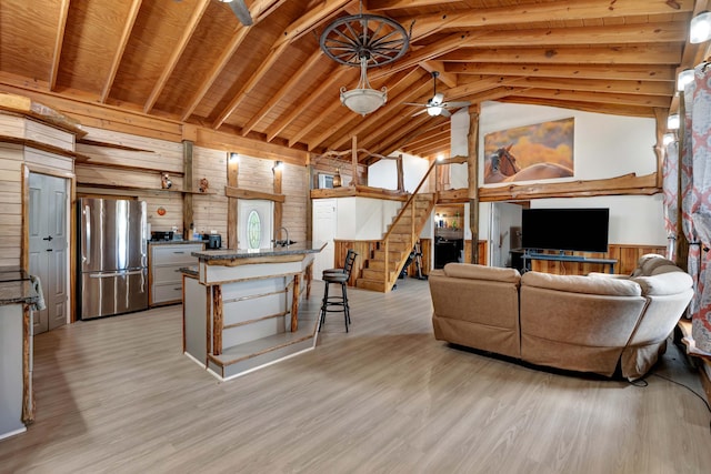 living room with wood walls, light hardwood / wood-style flooring, wooden ceiling, beamed ceiling, and ceiling fan