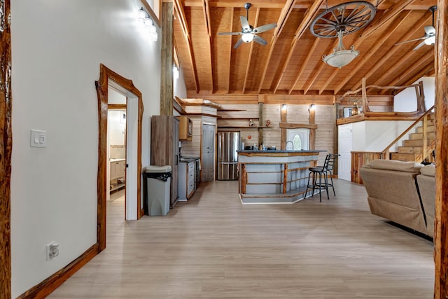 kitchen featuring wooden walls, stainless steel fridge, a kitchen bar, wood ceiling, and light hardwood / wood-style flooring