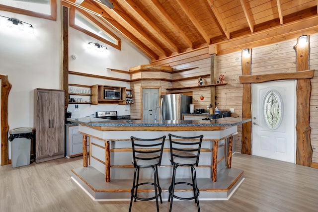 kitchen featuring appliances with stainless steel finishes, high vaulted ceiling, wooden walls, beamed ceiling, and light hardwood / wood-style floors