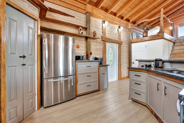 kitchen with white cabinetry, vaulted ceiling with beams, stainless steel fridge, and wood walls