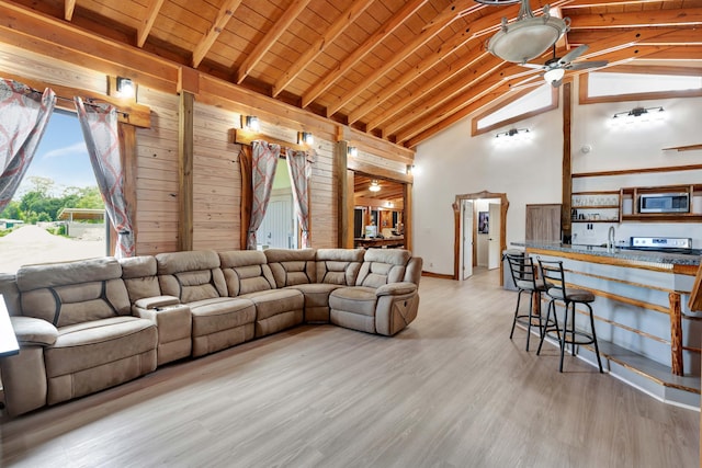 living room with high vaulted ceiling, beam ceiling, ceiling fan, wooden ceiling, and light wood-type flooring