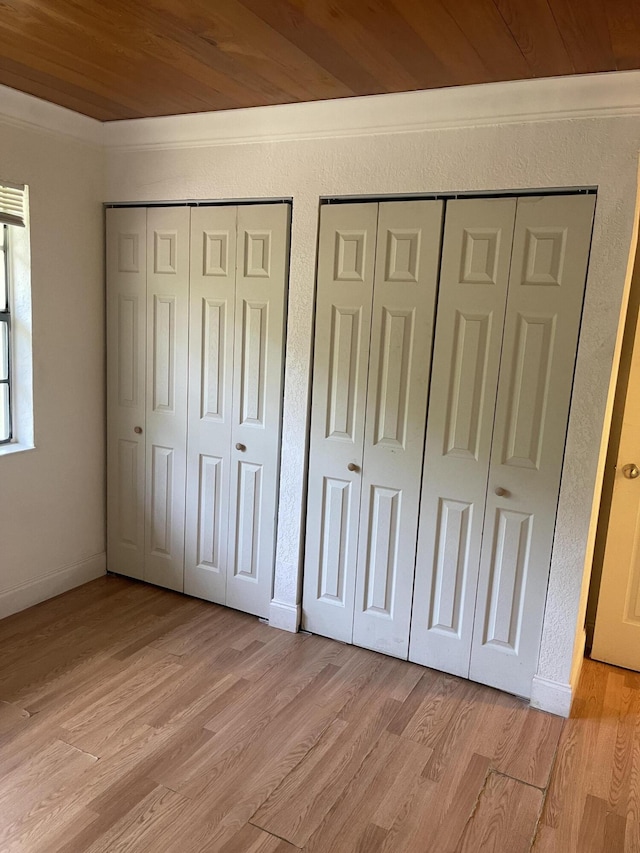 unfurnished bedroom featuring wooden ceiling, light hardwood / wood-style flooring, and two closets