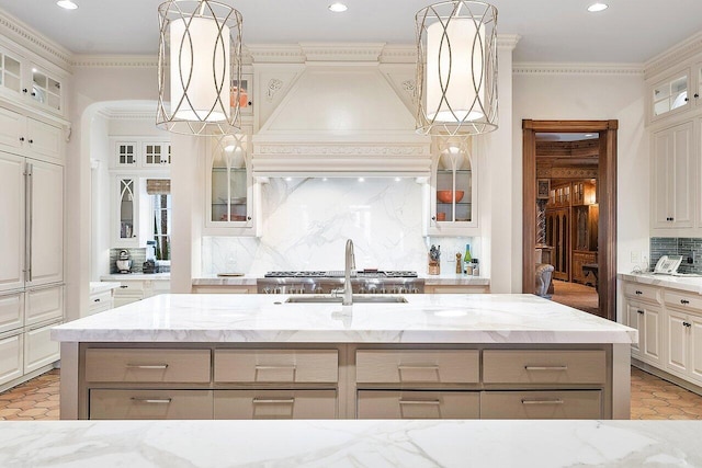 kitchen featuring premium range hood, light stone countertops, backsplash, and a kitchen island with sink