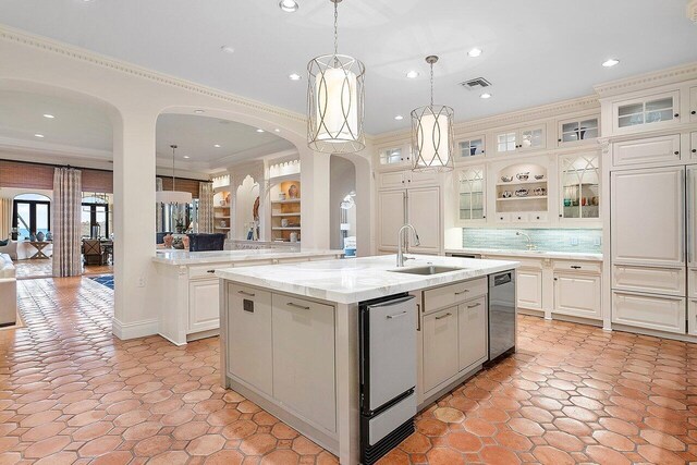 kitchen with light tile patterned flooring, pendant lighting, crown molding, sink, and a kitchen island with sink