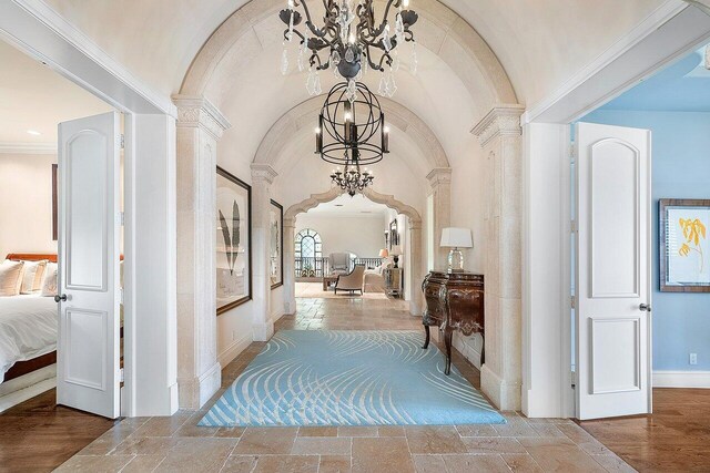 corridor with hardwood / wood-style flooring, a notable chandelier, ornate columns, and ornamental molding