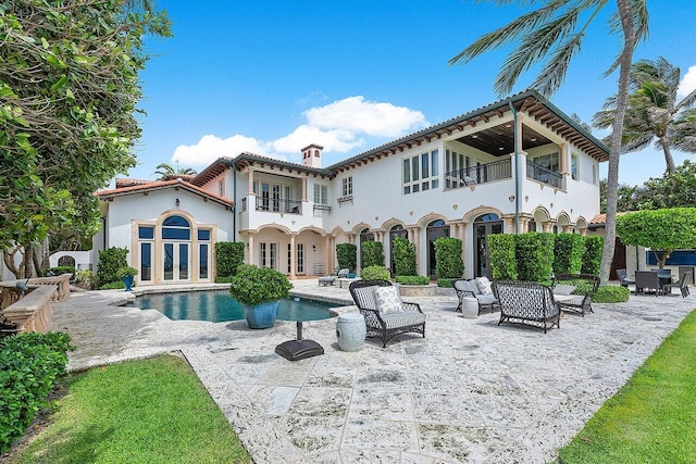 rear view of property with a balcony, a patio, a fenced in pool, and french doors