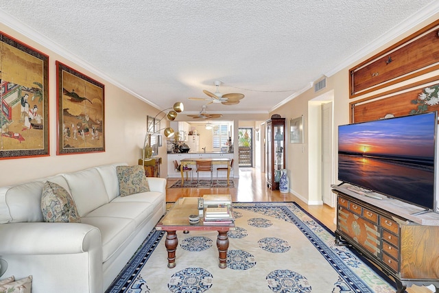 living room with a textured ceiling, light hardwood / wood-style floors, ceiling fan, and crown molding