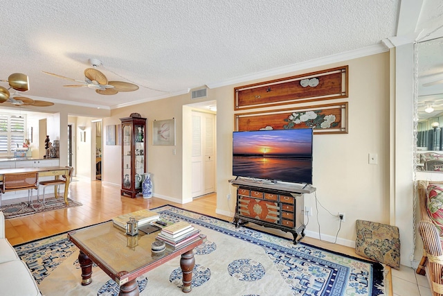 living room featuring ceiling fan, light hardwood / wood-style floors, a textured ceiling, and ornamental molding