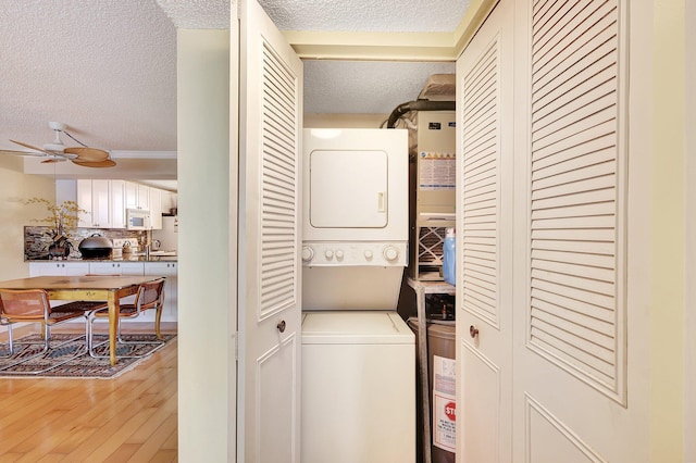 laundry area with a textured ceiling, hardwood / wood-style flooring, ceiling fan, and stacked washer and clothes dryer