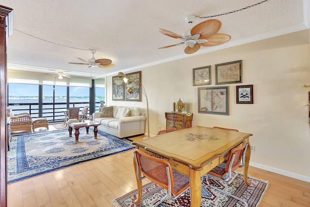 dining room featuring light wood-type flooring, a textured ceiling, a water view, and ornamental molding