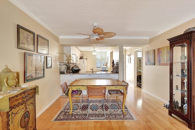 dining area with sink, light wood-type flooring, a textured ceiling, and ornamental molding