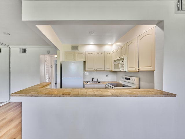 kitchen with kitchen peninsula, sink, white appliances, and light wood-type flooring