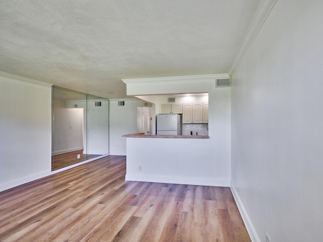 unfurnished living room featuring a textured ceiling, light wood-type flooring, and ornamental molding