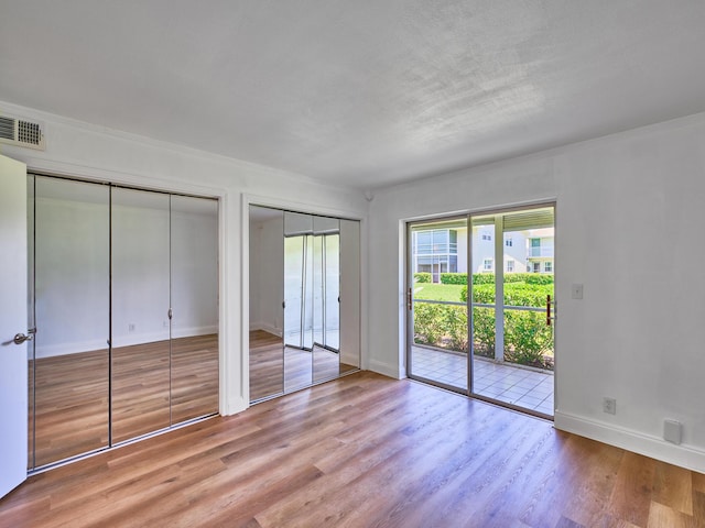 unfurnished bedroom featuring access to exterior, light hardwood / wood-style flooring, and two closets