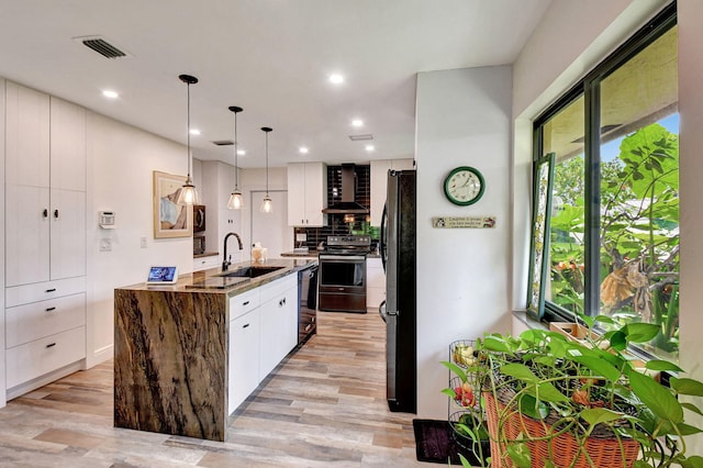 kitchen with black appliances, wall chimney range hood, white cabinetry, decorative light fixtures, and sink