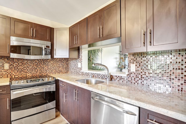 kitchen featuring decorative backsplash, stainless steel appliances, light stone counters, and sink