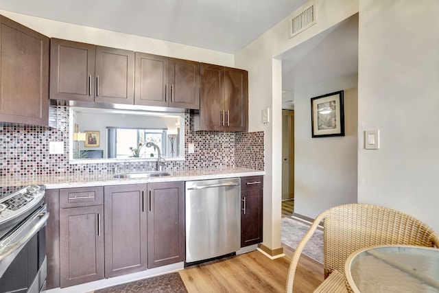 kitchen with backsplash, sink, light wood-type flooring, dark brown cabinets, and stainless steel appliances