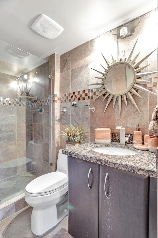 bathroom with tasteful backsplash, toilet, tiled shower, vanity, and tile walls