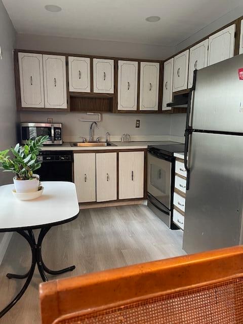 kitchen with black appliances, sink, light hardwood / wood-style flooring, and white cabinets