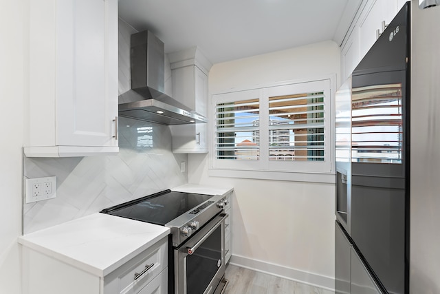 kitchen featuring tasteful backsplash, white cabinets, light wood-type flooring, wall chimney exhaust hood, and stainless steel stove