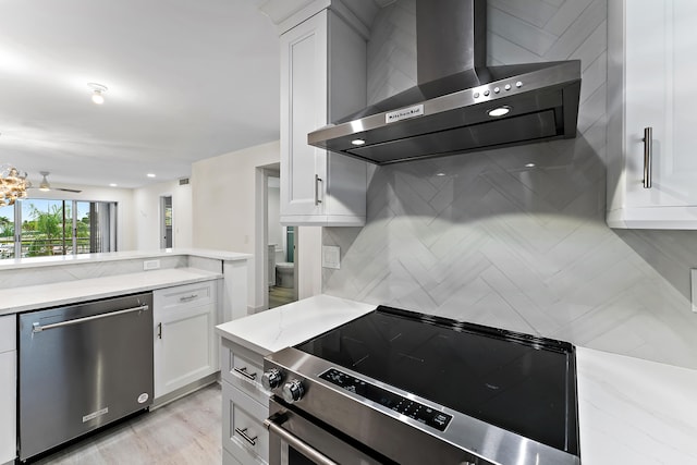 kitchen with tasteful backsplash, white cabinets, wall chimney exhaust hood, appliances with stainless steel finishes, and light hardwood / wood-style flooring