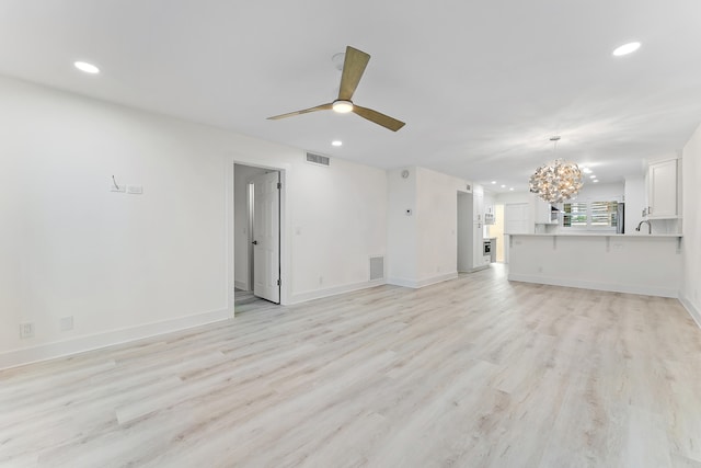 unfurnished living room with ceiling fan with notable chandelier, sink, and light wood-type flooring