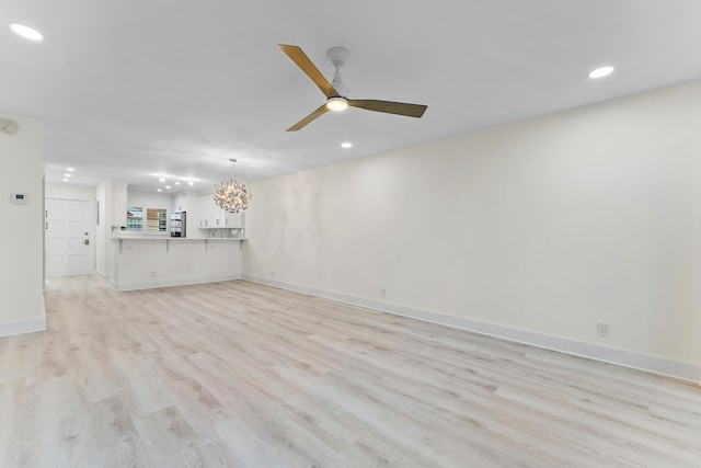 unfurnished living room with ceiling fan with notable chandelier and light hardwood / wood-style flooring