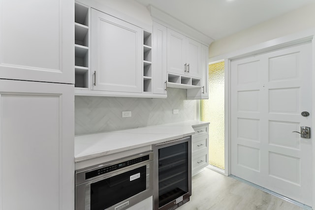 kitchen featuring white cabinets, beverage cooler, backsplash, light hardwood / wood-style floors, and oven