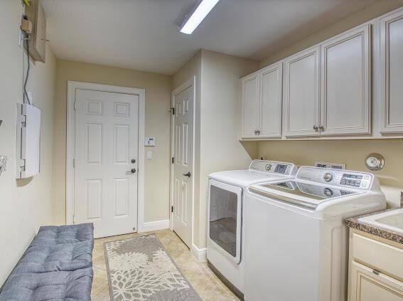 clothes washing area featuring cabinets, washing machine and clothes dryer, electric panel, and light tile patterned floors