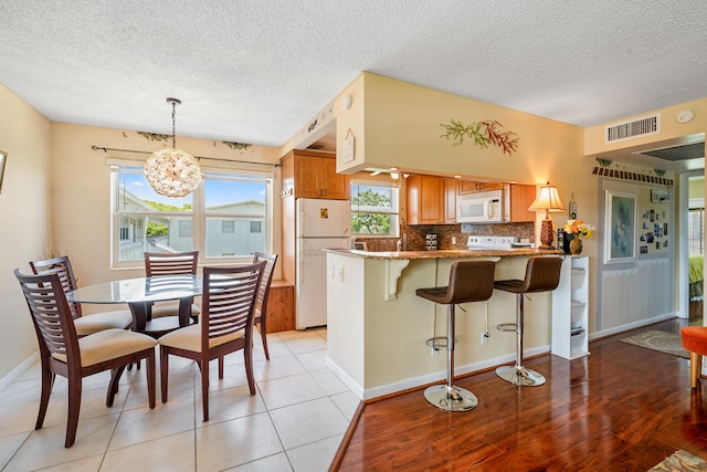 kitchen with kitchen peninsula, white appliances, light tile flooring, backsplash, and a chandelier