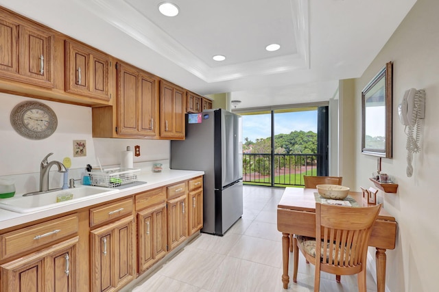 kitchen with a tray ceiling, ornamental molding, stainless steel fridge, sink, and light tile patterned floors