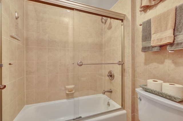 bathroom featuring toilet, combined bath / shower with glass door, and tile walls