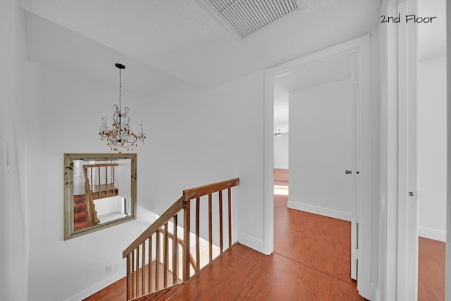 corridor featuring a textured ceiling, hardwood / wood-style flooring, and an inviting chandelier