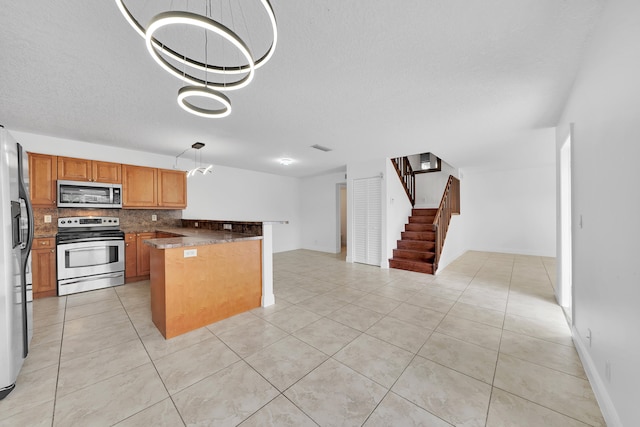 kitchen featuring stainless steel appliances, kitchen peninsula, a chandelier, pendant lighting, and decorative backsplash