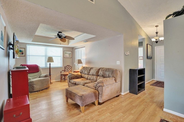 living room featuring light wood-type flooring, a textured ceiling, ceiling fan with notable chandelier, and a tray ceiling