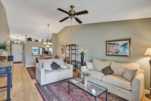 living area featuring lofted ceiling, ceiling fan with notable chandelier, baseboards, and light wood-style floors