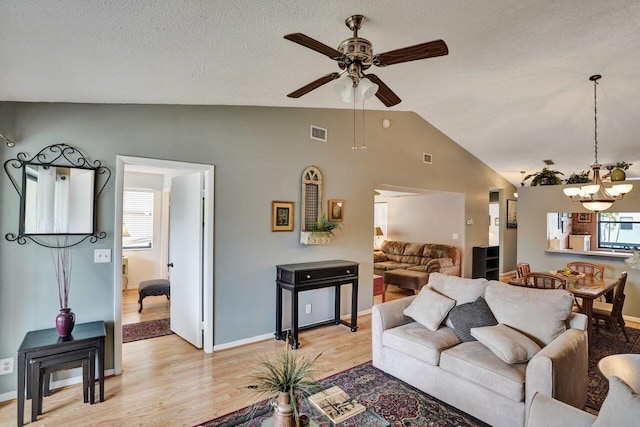 living room featuring visible vents, vaulted ceiling, a textured ceiling, light wood-style floors, and ceiling fan with notable chandelier