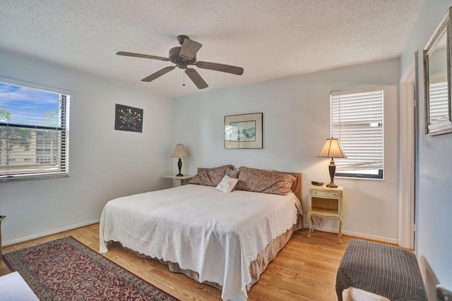 bedroom with multiple windows, ceiling fan, light hardwood / wood-style flooring, and a textured ceiling