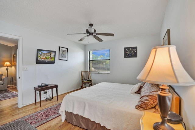 bedroom featuring light wood-type flooring, a textured ceiling, baseboards, and a ceiling fan