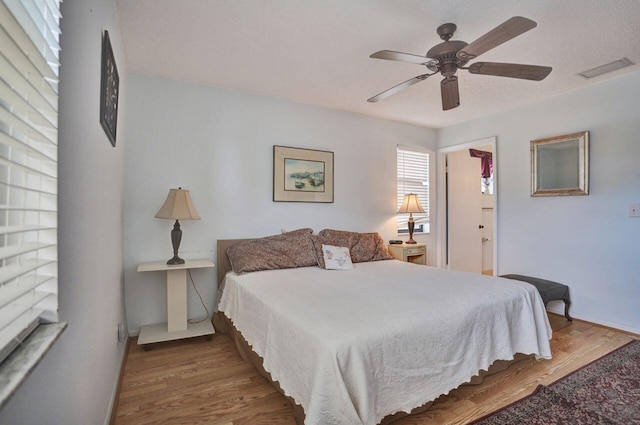 bedroom with a textured ceiling, visible vents, wood finished floors, and a ceiling fan