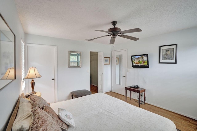 bedroom with ceiling fan, a textured ceiling, baseboards, and wood finished floors