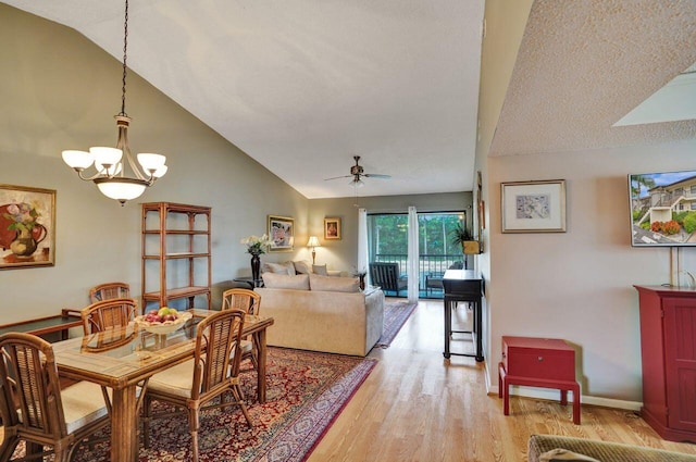 dining room featuring ceiling fan with notable chandelier, light wood-type flooring, and vaulted ceiling