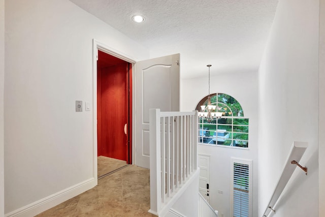 hallway featuring an inviting chandelier and a textured ceiling